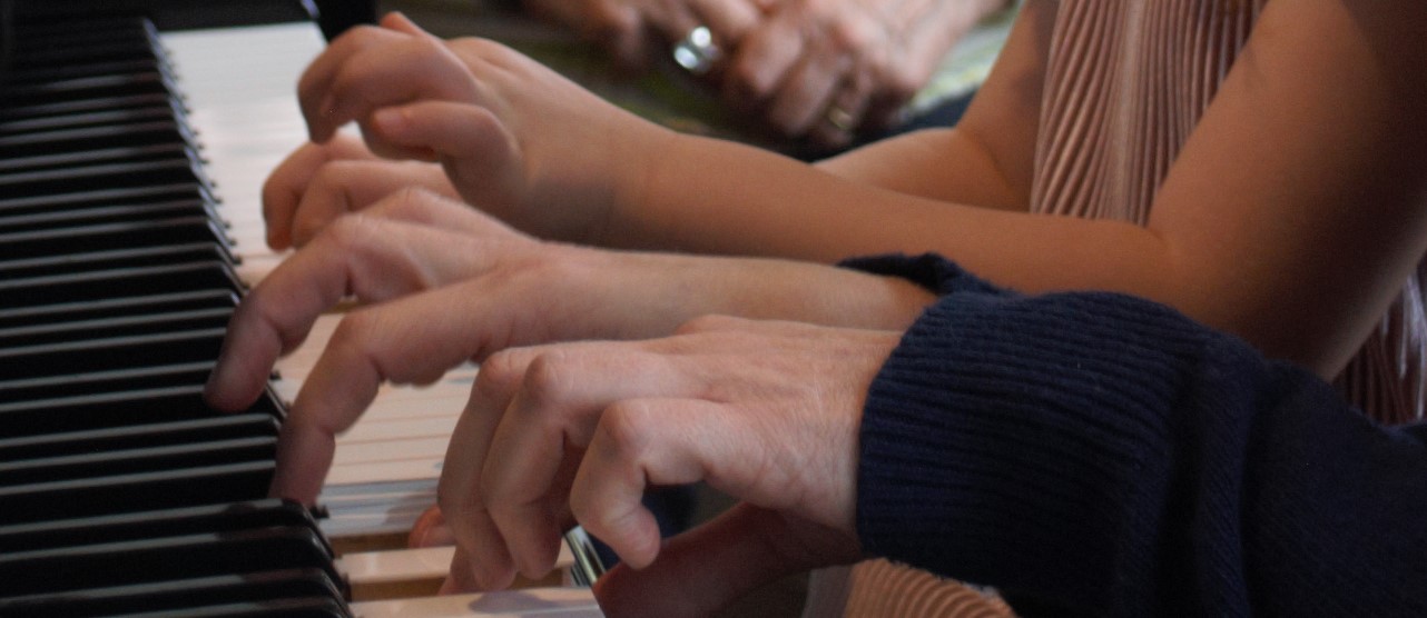kleuterhanden en de handen van juf bespelen samen de pianotoetsen